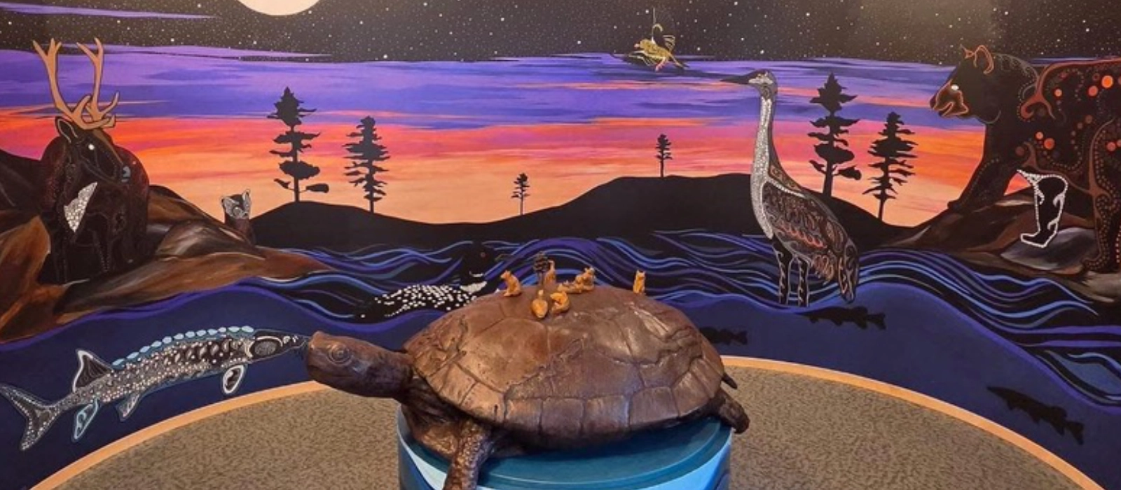 A turtle sculpture before an illustrated Northwoods landscape in the Zagaandagaa-Anishinaabeg exhibit